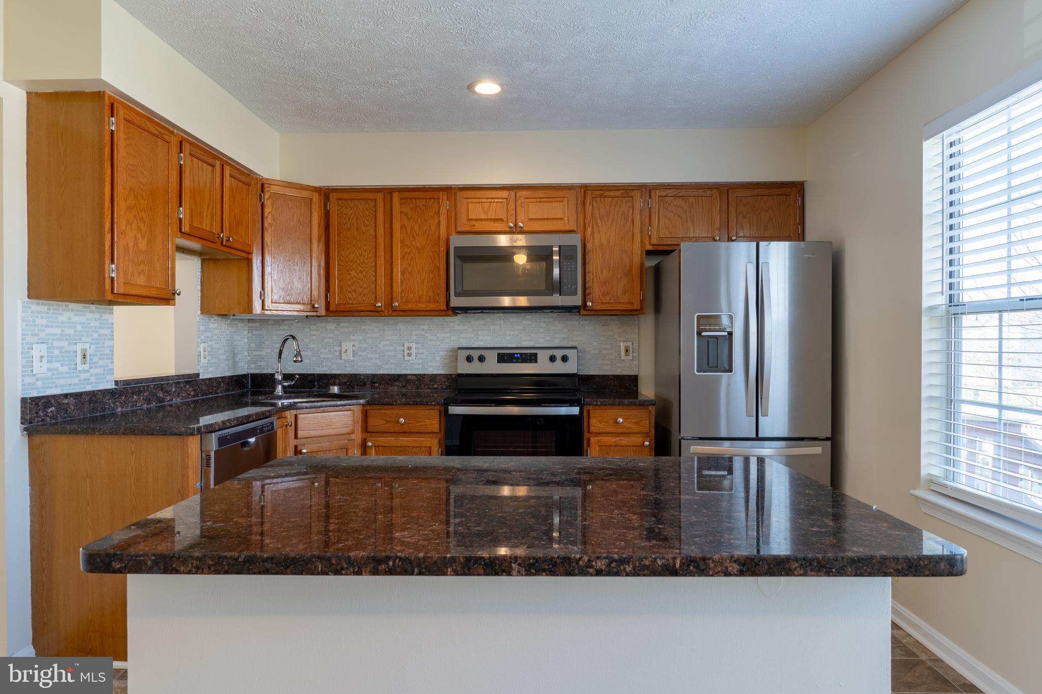 224 Oak Leaf Way Halethorpe, MD 21227 - Photo 9 of 32 a kitchen with stainless steel appliances granite countertop a refrigerator a stove and a sink with wooden cabinets