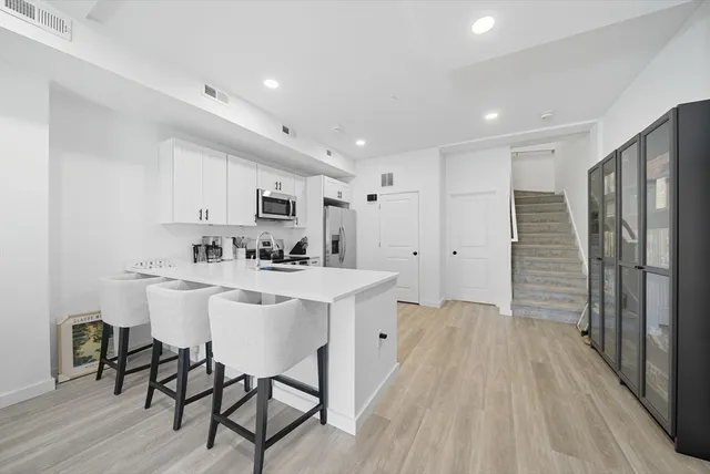 a kitchen with stainless steel appliances granite countertop a sink a stove a refrigerator and white cabinets with wooden floor