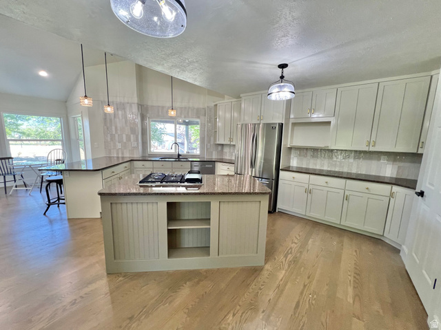 812 East Bates Cyn Road Tooele, UT 84074 - Photo 21 of 144 Open-concept kitchen featuring an expansive center island with a built-in cooktop, light-toned wood-finish flooring, white cabinetry with gold-tone hardware, and a tile backsplash