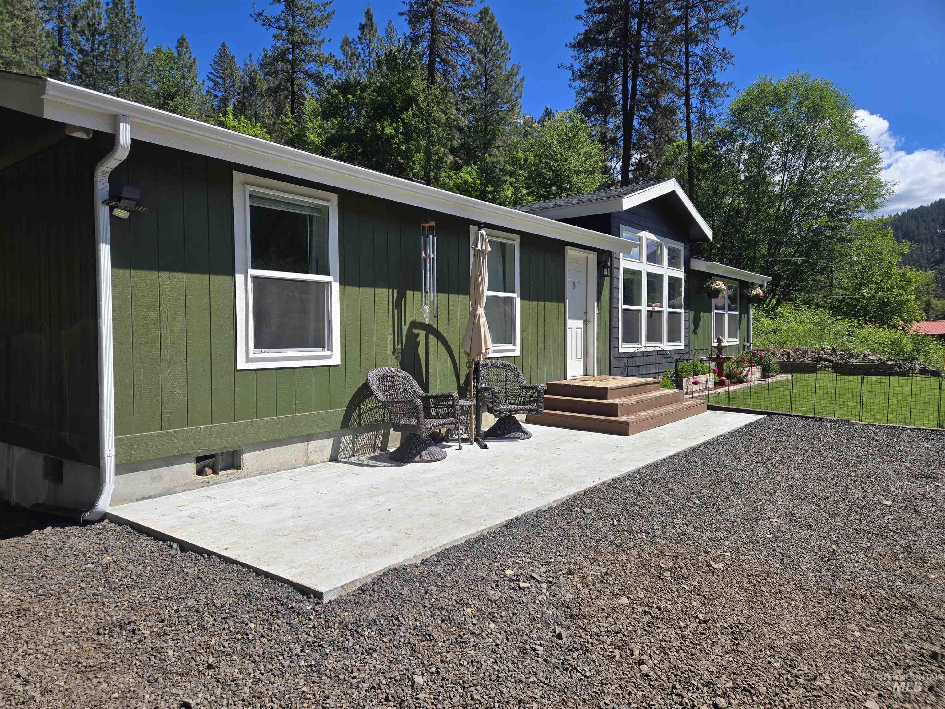 174 Konkolville Road Orofino, ID 83544 - Photo 41 of 43 Exterior featuring vertical panel siding, white-trimmed windows, a concrete patio, a gravel driveway, and a fenced yard area