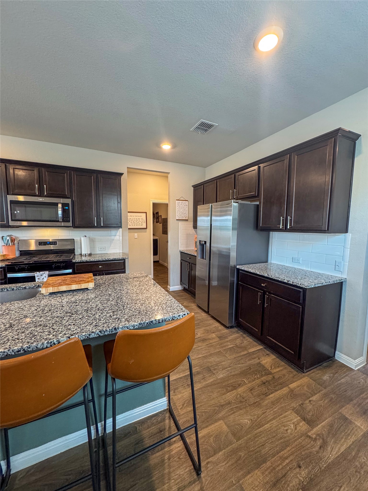 107 Hamilton Pool Lane Bastrop, TX 78602 - Photo 7 of 22 Kitchen featuring dark wood finish cabinetry, light stone countertops, stainless steel appliances, and recessed lighting.