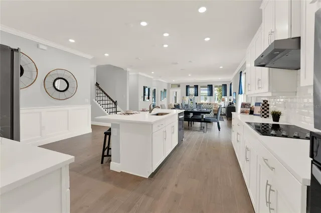 a large white kitchen with a stove a sink a refrigerator and a dining table with wooden floor