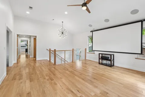 a view of an empty room with wooden floor and a ceiling fan
