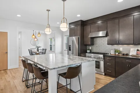 a kitchen with stainless steel appliances granite countertop a stove a sink dishwasher a dining table and chairs with wooden floor