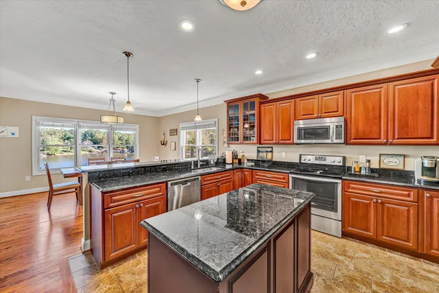 a kitchen with stainless steel appliances granite countertop a stove top oven a refrigerator a dining table and chairs with wooden floor