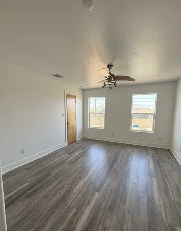 an empty room with wooden floor chandelier and windows