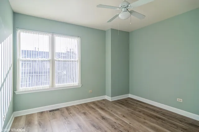 an empty room with wooden floor windows and fan
