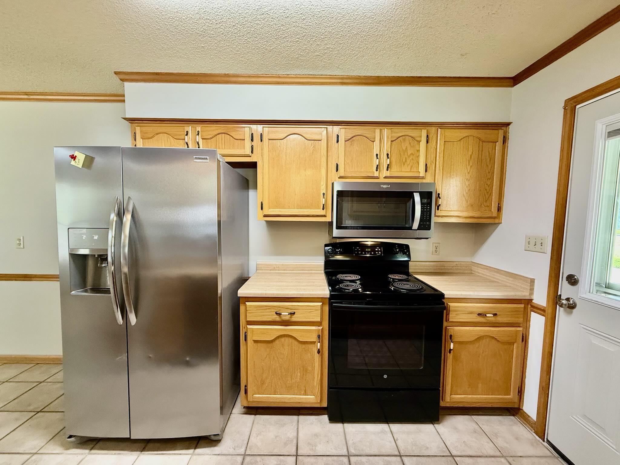2151 Bartlett Road Memphis, TN 38134 - Photo 11 of 27 Kitchen featuring stainless steel appliances, light countertops, light tile patterned floors, crown molding, and a textured ceiling