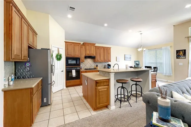 a kitchen with stainless steel appliances kitchen island granite countertop a refrigerator a stove a sink a dining table and chairs with wooden floor