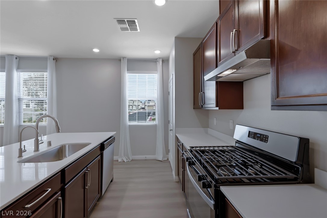 3564 Credere Lane Henderson, NV 89074 - Photo 10 of 40 Kitchen featuring stainless steel appliances, dark wood finish cabinetry, recessed lighting, light stone countertops, and light wood-style floors
