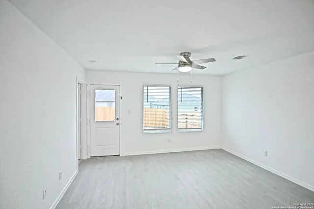 an empty room with chandelier fan and windows