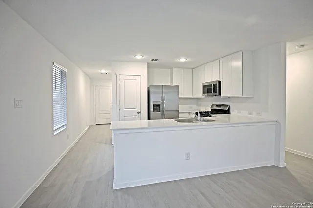 a kitchen with stainless steel appliances granite countertop a stove a sink a refrigerator white cabinets and wooden floor