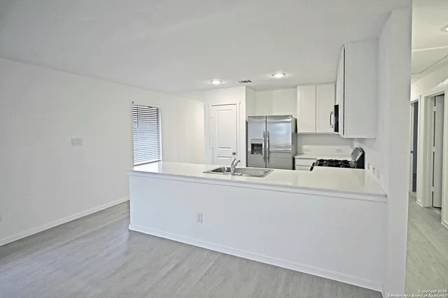 a kitchen with stainless steel appliances granite countertop a sink a stove a refrigerator with white cabinets and wooden floor