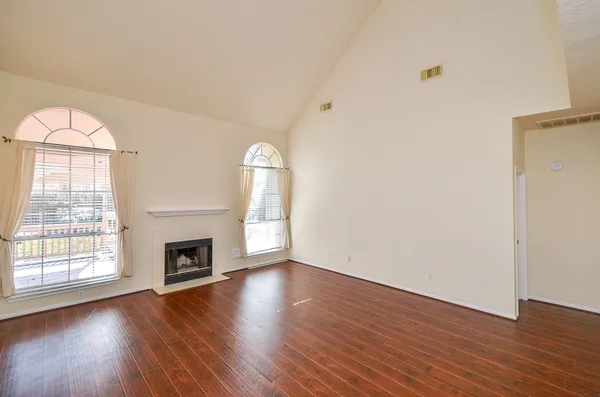 an empty room with wooden floor fireplace and windows