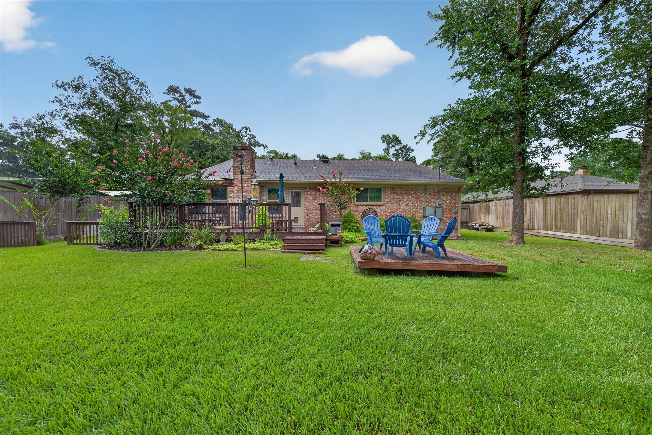 24719 Wilderness Road Spring, TX 77380 - Photo 40 of 42 This photo showcases a spacious backyard featuring a lush green lawn, a mature tree, and a wooden deck area. The area is enclosed by a wooden fence, providing privacy and a serene outdoor space ideal for relaxation or entertaining.