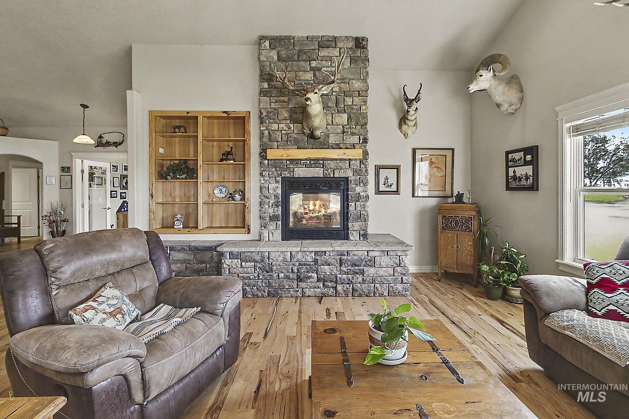 6900 West Charters Lane Melba, ID 83641 - Photo 10 of 49 Central stone-faced fireplace with a hearth, wood-finish flooring, built-in shelving, vaulted ceiling, and a large window