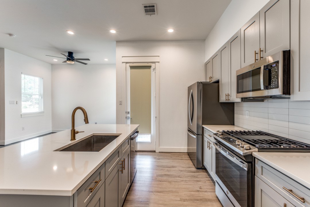 728 East 38th Street Houston, TX 77022 - Photo 5 of 18 Bright and modern kitchen featuring stainless steel appliances, a large island with sink, recessed lighting, and open flow to the dining and living spaces.