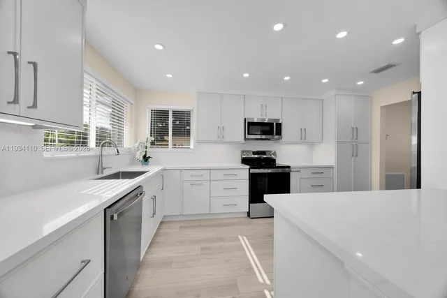 a large kitchen with cabinets stainless steel appliances a sink and a window
