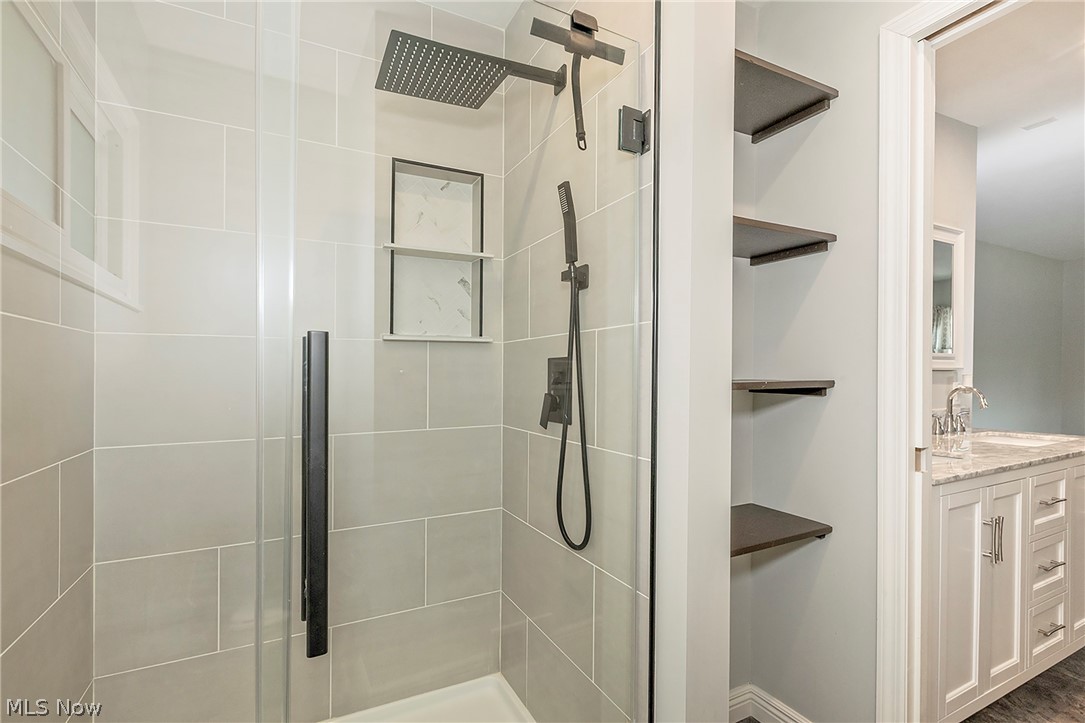 3719 Walter Road North Olmsted, OH 44070 - Photo 21 of 35 Walk-in shower with light gray tile surround, rainfall showerhead, integrated shelving, and dark bronze fixtures