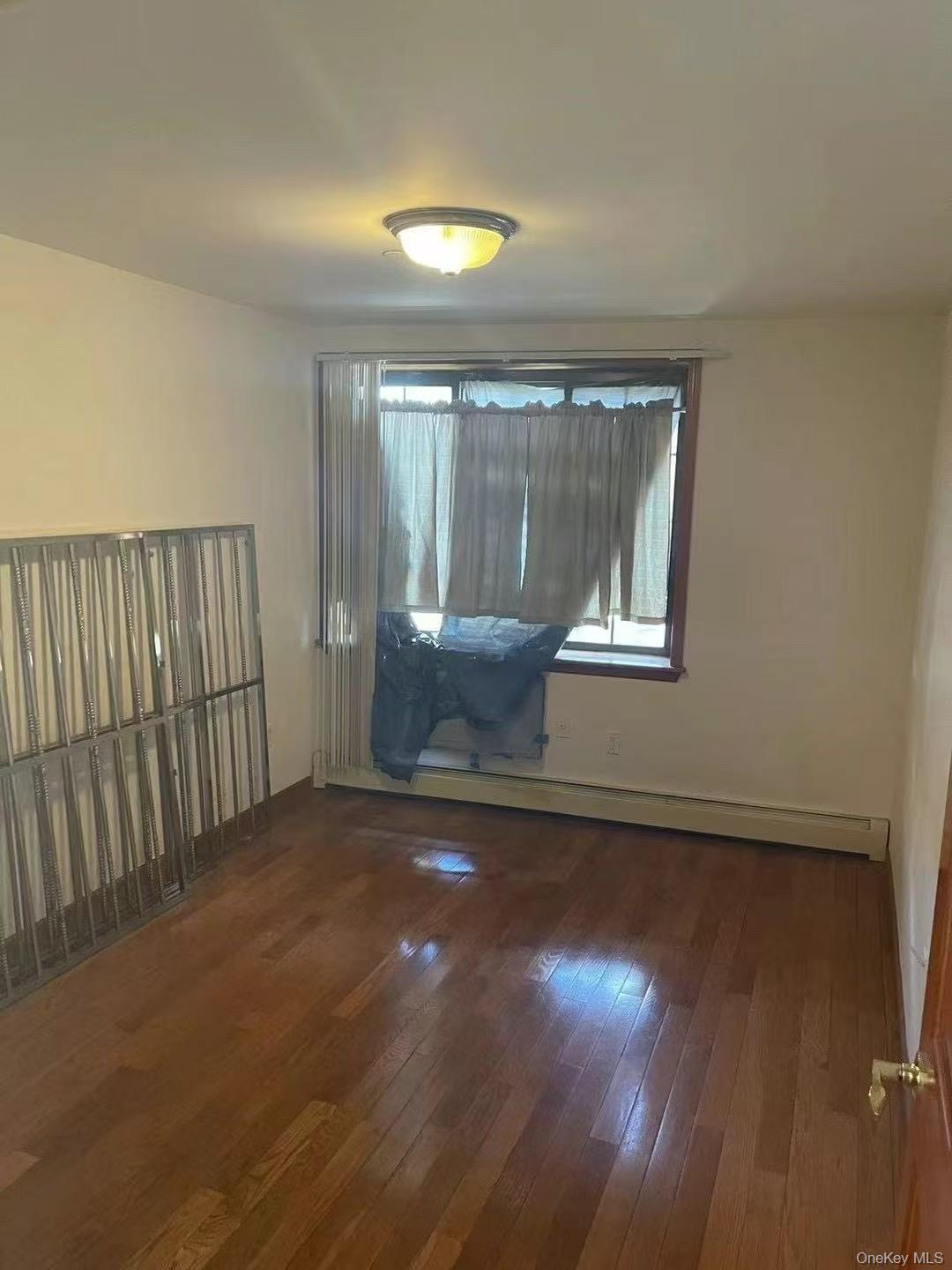 109-15 Westside Avenue, Unit 1A Queens, NY 11368 - Photo 4 of 8 Empty room with dark wood-style floors and a baseboard heating unit
