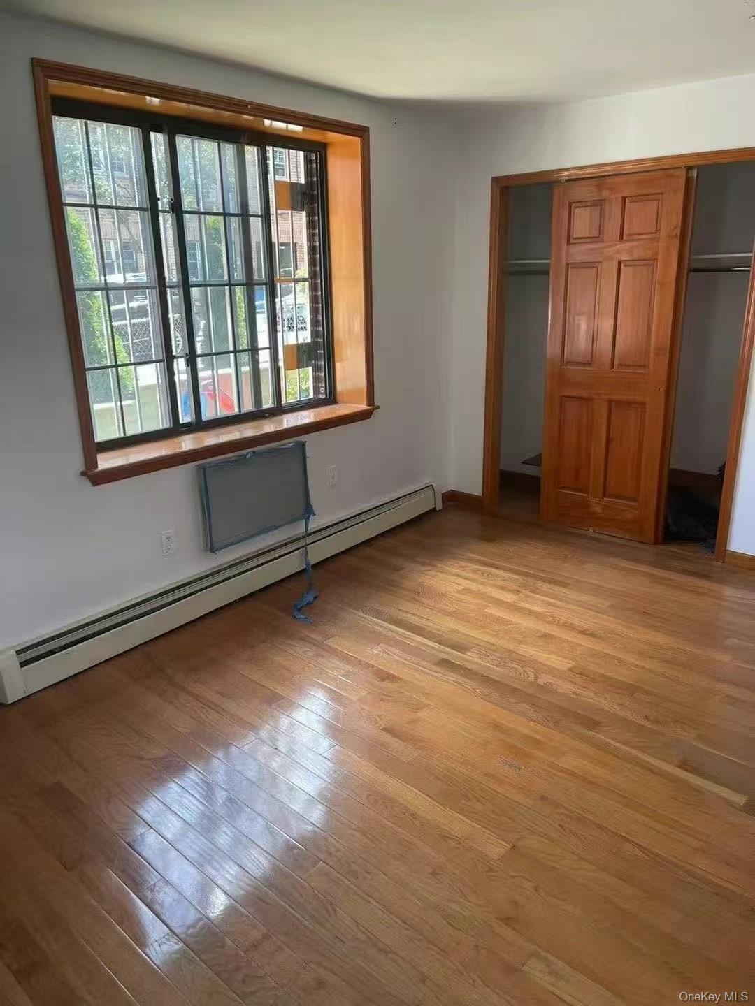 109-15 Westside Avenue, Unit 1A Queens, NY 11368 - Photo 5 of 8 Unfurnished bedroom with a baseboard radiator, light wood finished floors, and a closet