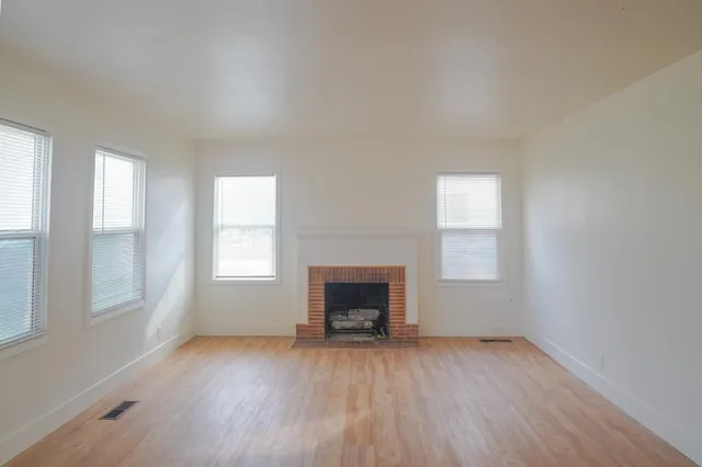 an empty room with wooden floor fireplace and windows