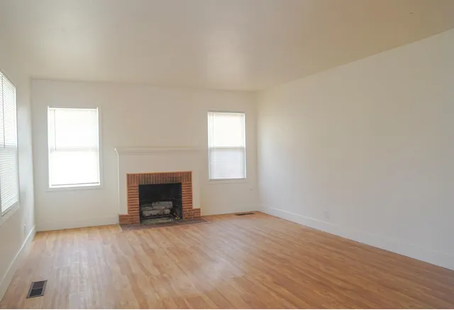 an empty room with wooden floor fireplace and windows