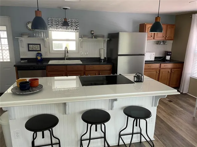 a kitchen with stainless steel appliances kitchen island granite countertop a dining table chairs and a refrigerator