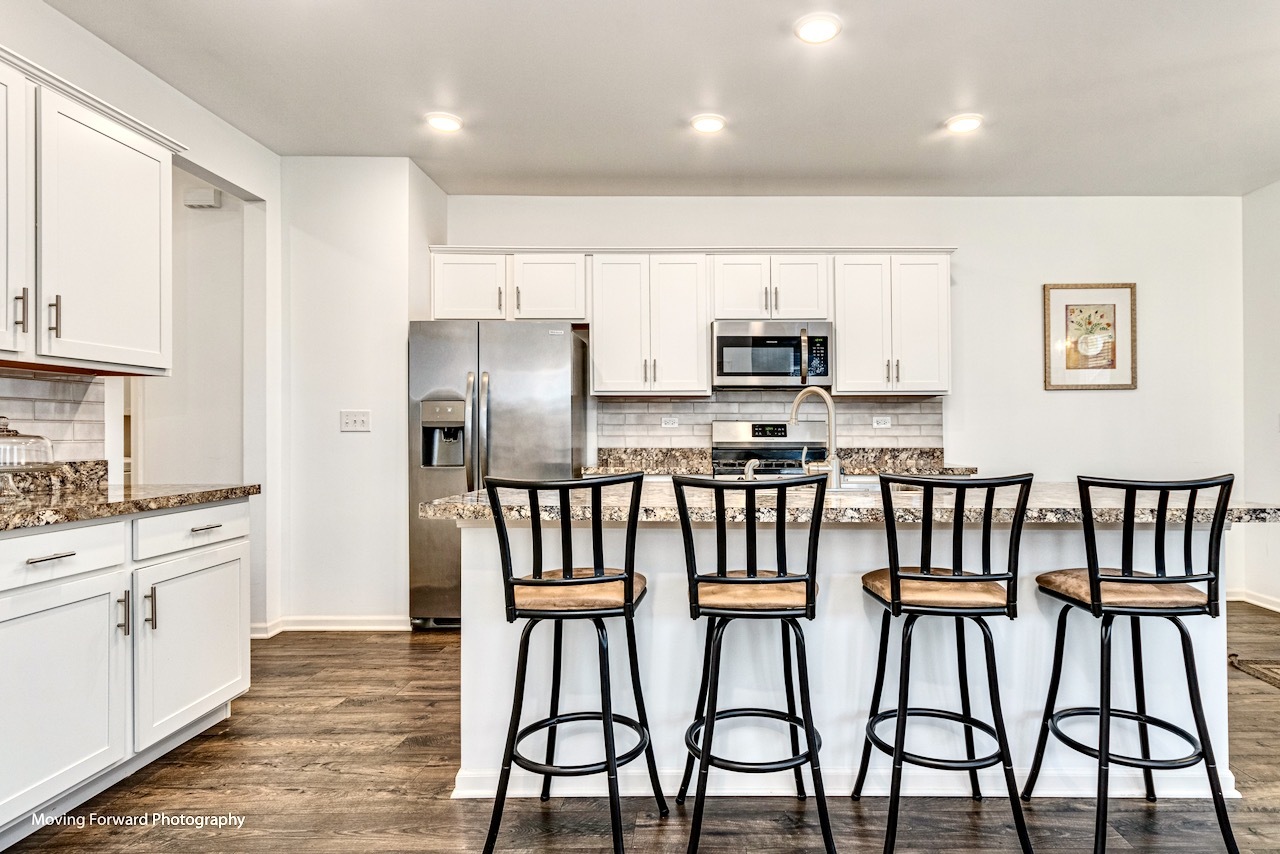 1908 Southern Circle, Unit 1908 Pingree Grove, IL 60140 - Photo 9 of 30 a kitchen with stainless steel appliances kitchen island granite countertop a table chairs microwave and sink