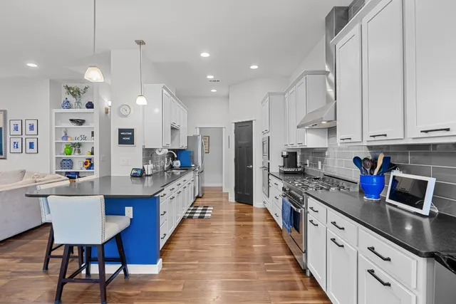 a large kitchen with stainless steel appliances a sink a stove a refrigerator a kitchen island with chairs and white cabinets