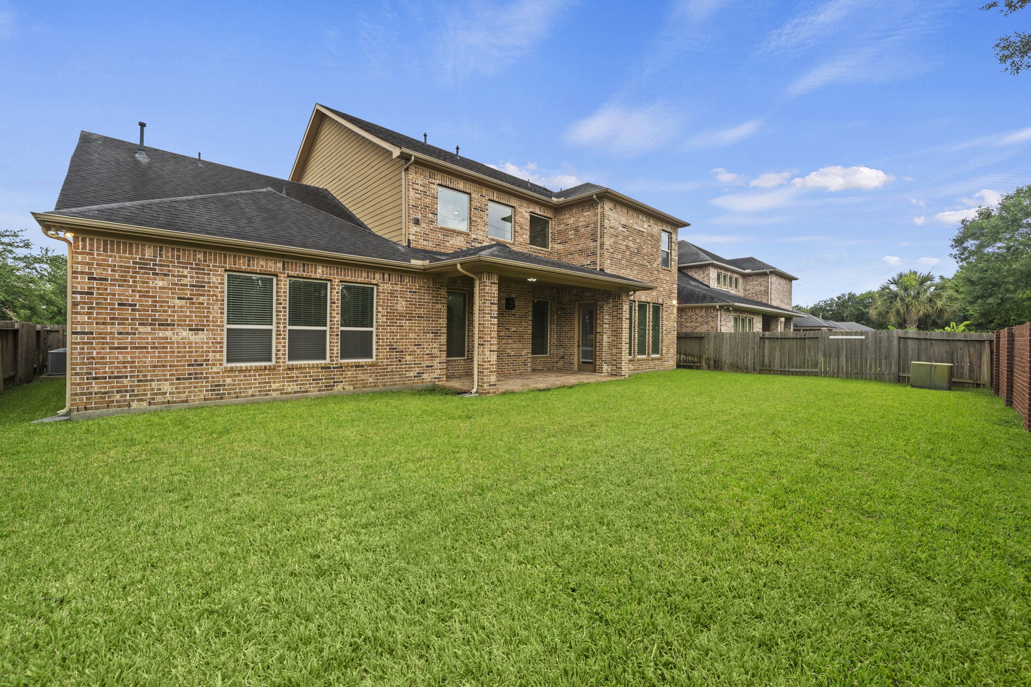 14215 Spindle Arbor Road Cypress, TX 77429 - Photo 42 of 47 This photo shows a spacious backyard with a well-maintained lawn, bordered by a wooden fence, and a two-story brick house featuring a covered patio. Ideal for outdoor activities and relaxation.