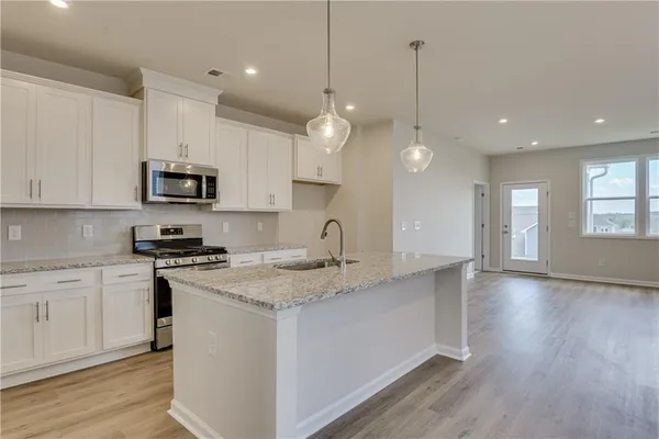 a kitchen with stainless steel appliances granite countertop a sink a stove a refrigerator and white cabinets with wooden floor