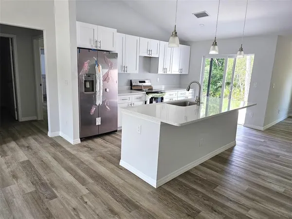 a kitchen with stainless steel appliances granite countertop a refrigerator a sink dishwasher a stove and white countertops with wooden floor