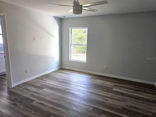 an empty room with wooden floor chandelier fan and windows