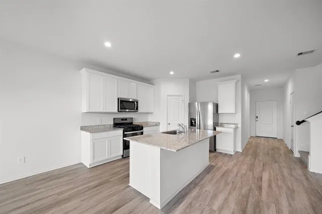 a large white kitchen with stainless steel appliances granite countertop a stove and a wooden floors