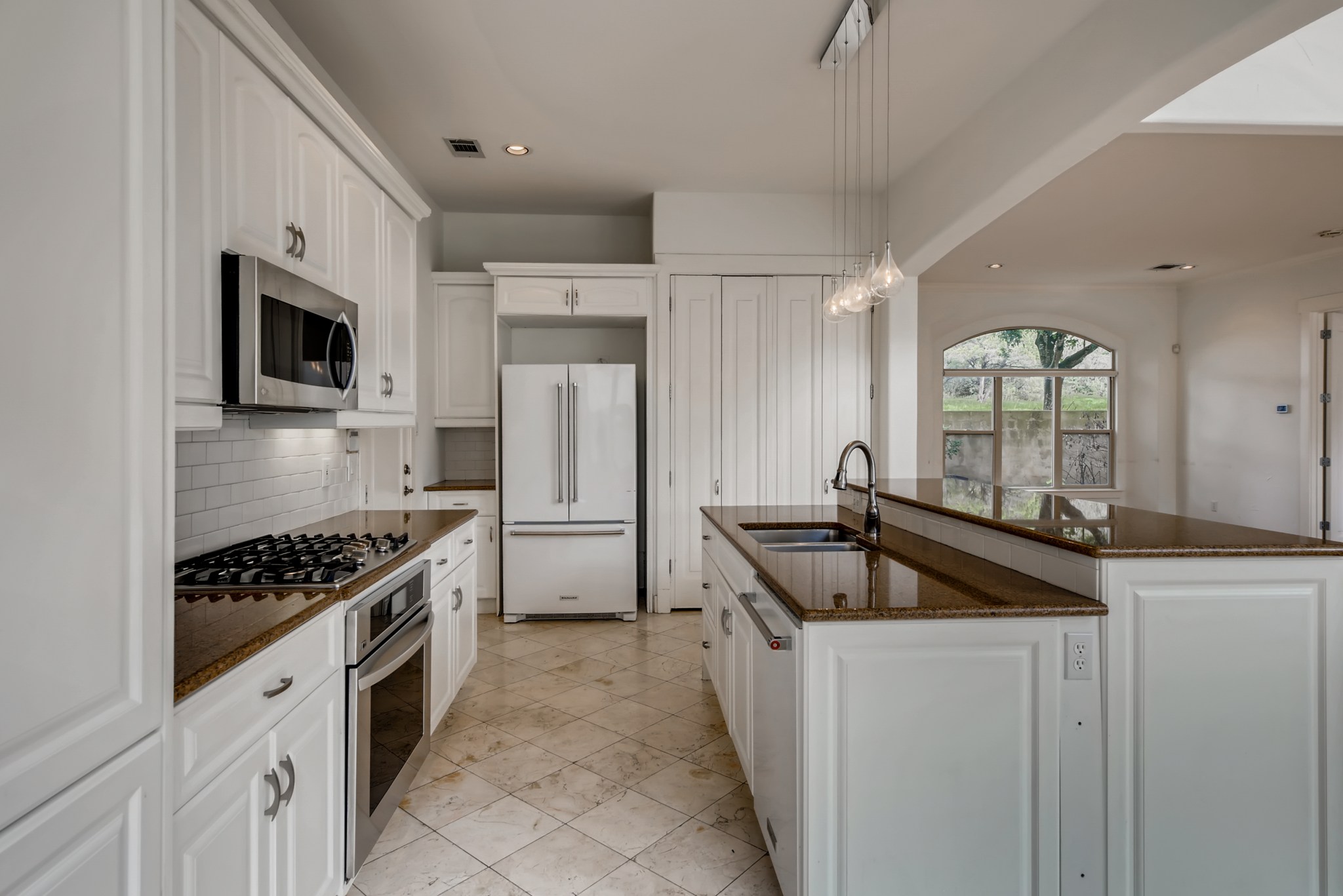 2800 Waymaker Way, Unit 27 Austin, TX 78746 - Photo 5 of 17 Kitchen featuring stainless steel appliances, white cabinets, a center island with sink, dark stone counters, and decorative light fixtures
