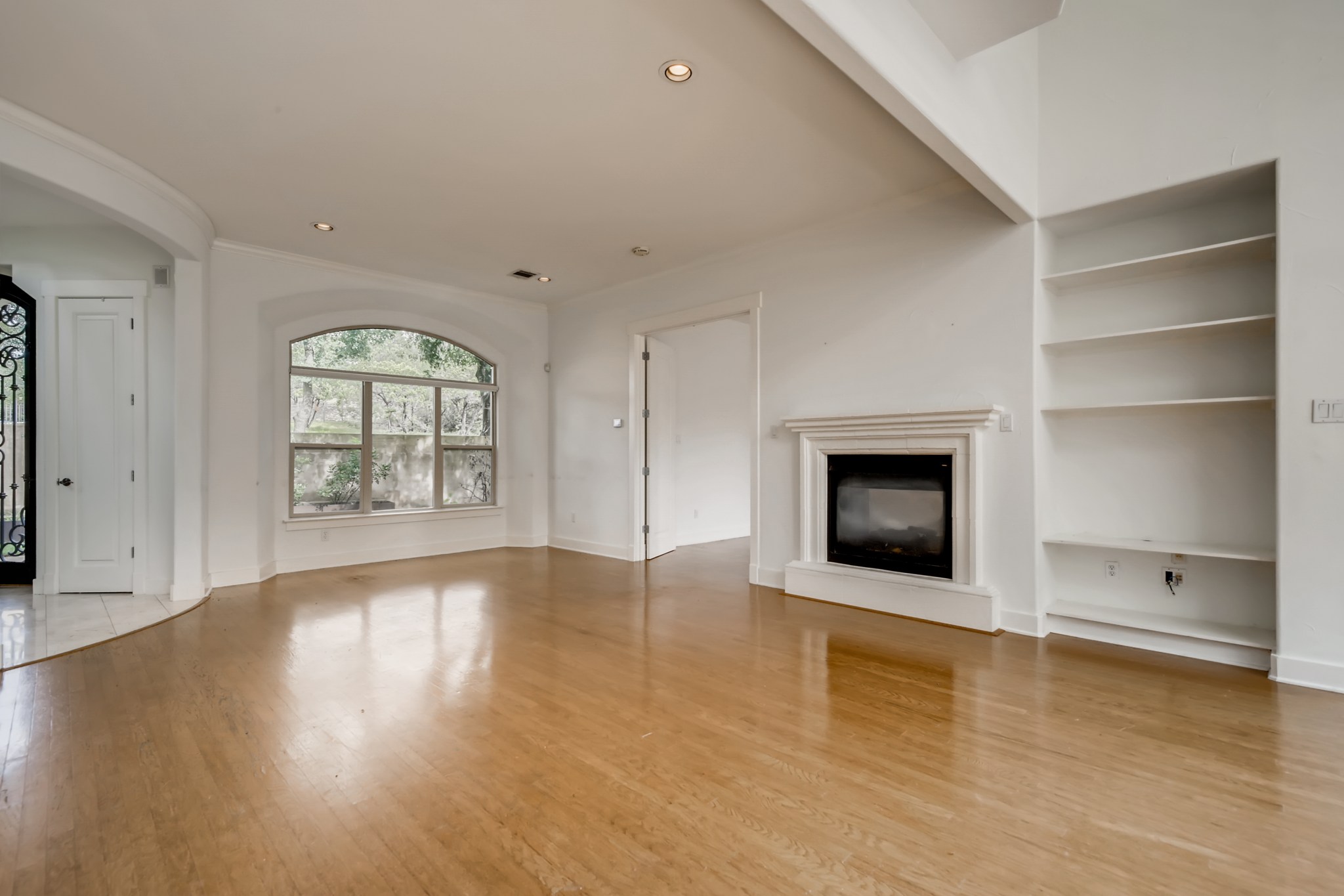 2800 Waymaker Way, Unit 27 Austin, TX 78746 - Photo 8 of 17 Unfurnished living room featuring a glass covered fireplace, light wood-style flooring, recessed lighting, built in shelves, and arched walkways