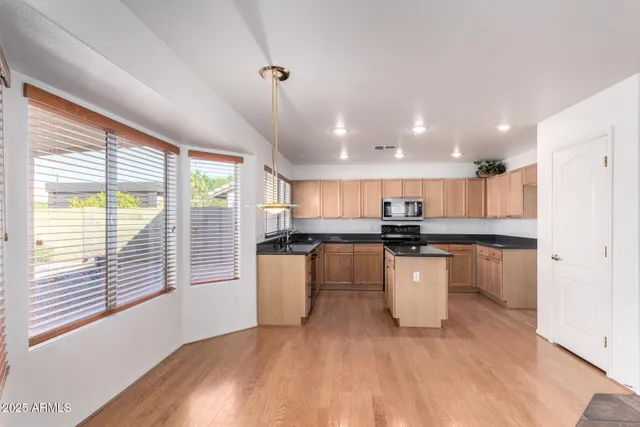 a kitchen with kitchen island granite countertop a sink a counter space stainless steel appliances cabinets and a large window