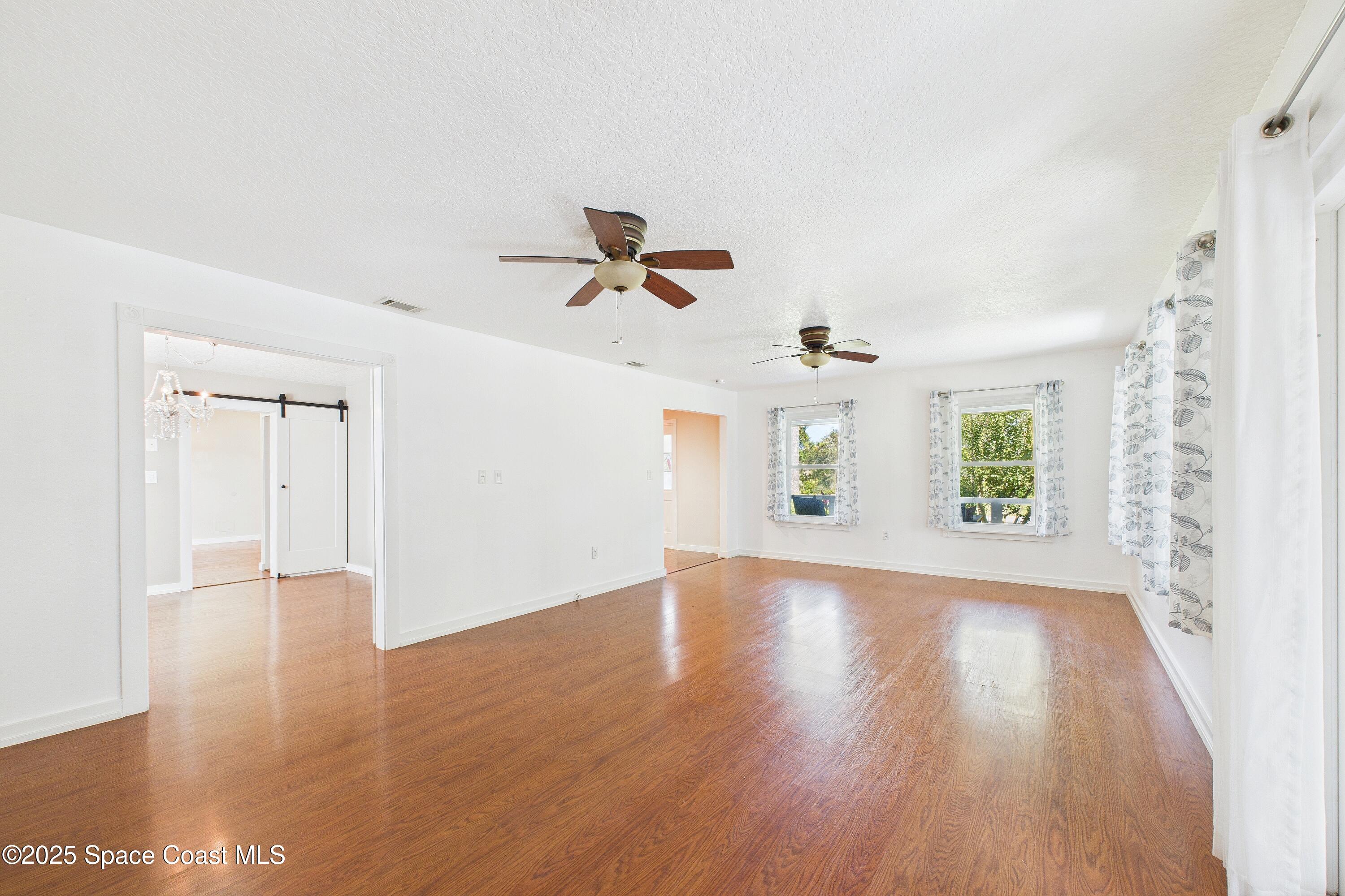 3435 Huggins Drive Malabar, FL 32950 - Photo 15 of 63 an empty room with wooden floor chandelier fan and windows