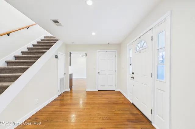 an empty room with wooden floor chandelier fan and windows