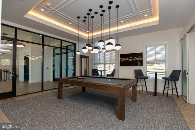 a living room with couches a chandelier with pool table and windows