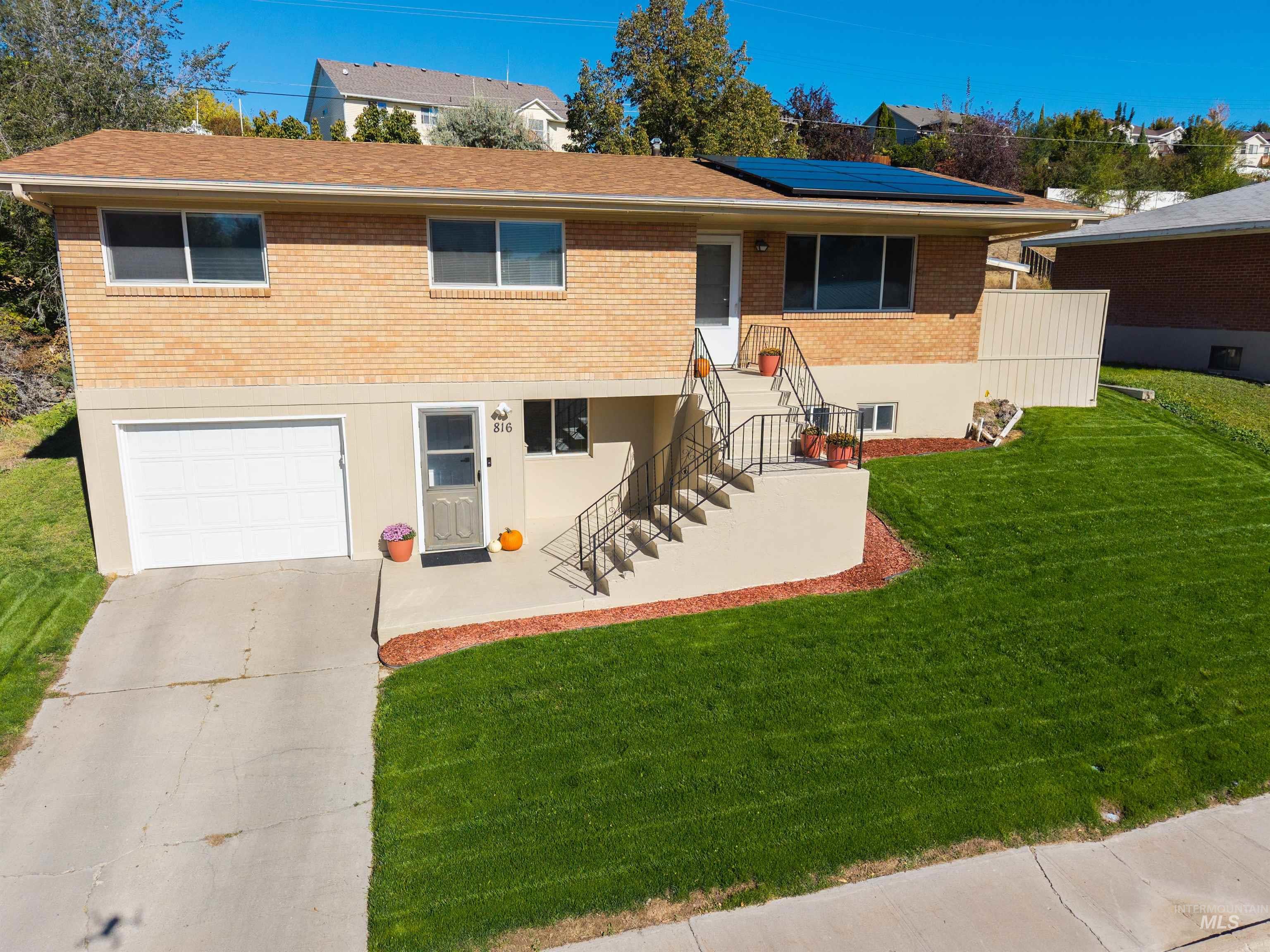 816 Park Lane Pocatello, ID 83201 - Photo 4 of 48 View of front of property featuring brick siding, a front yard, roof mounted solar panels, driveway, and a garage