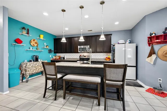 a kitchen with stainless steel appliances granite countertop a dining table chairs refrigerator and microwave