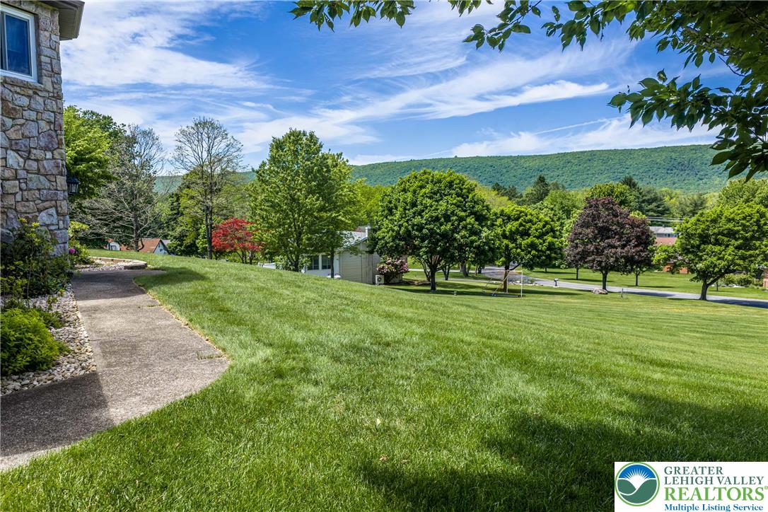 947 Tamenend Road Bath, PA 18014 - Photo 48 of 61 A verdant hillside property with a neatly kept lawn descends towards a tranquil, tree-lined landscape.