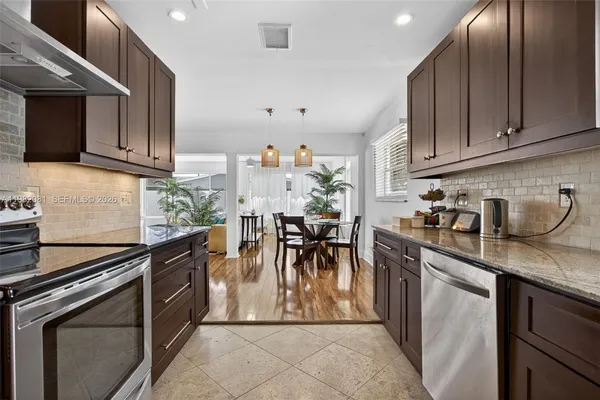 a kitchen with stainless steel appliances granite countertop a stove top oven a sink a dining table and chairs