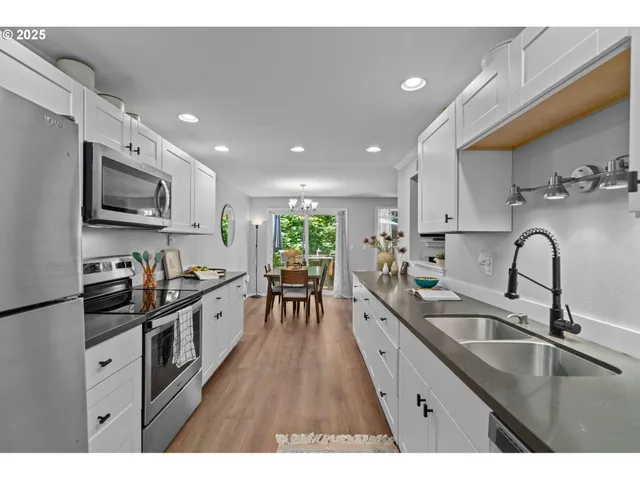 a kitchen with stainless steel appliances kitchen island granite countertop a stove a sink a microwave a dining table and chairs with wooden floor
