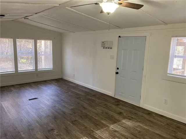 an empty room with wooden floor fan and windows