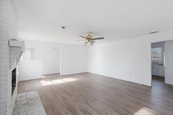 an empty room with wooden floor a ceiling fan and windows
