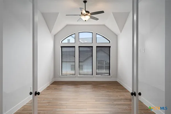an empty room with wooden floor chandelier fan and windows