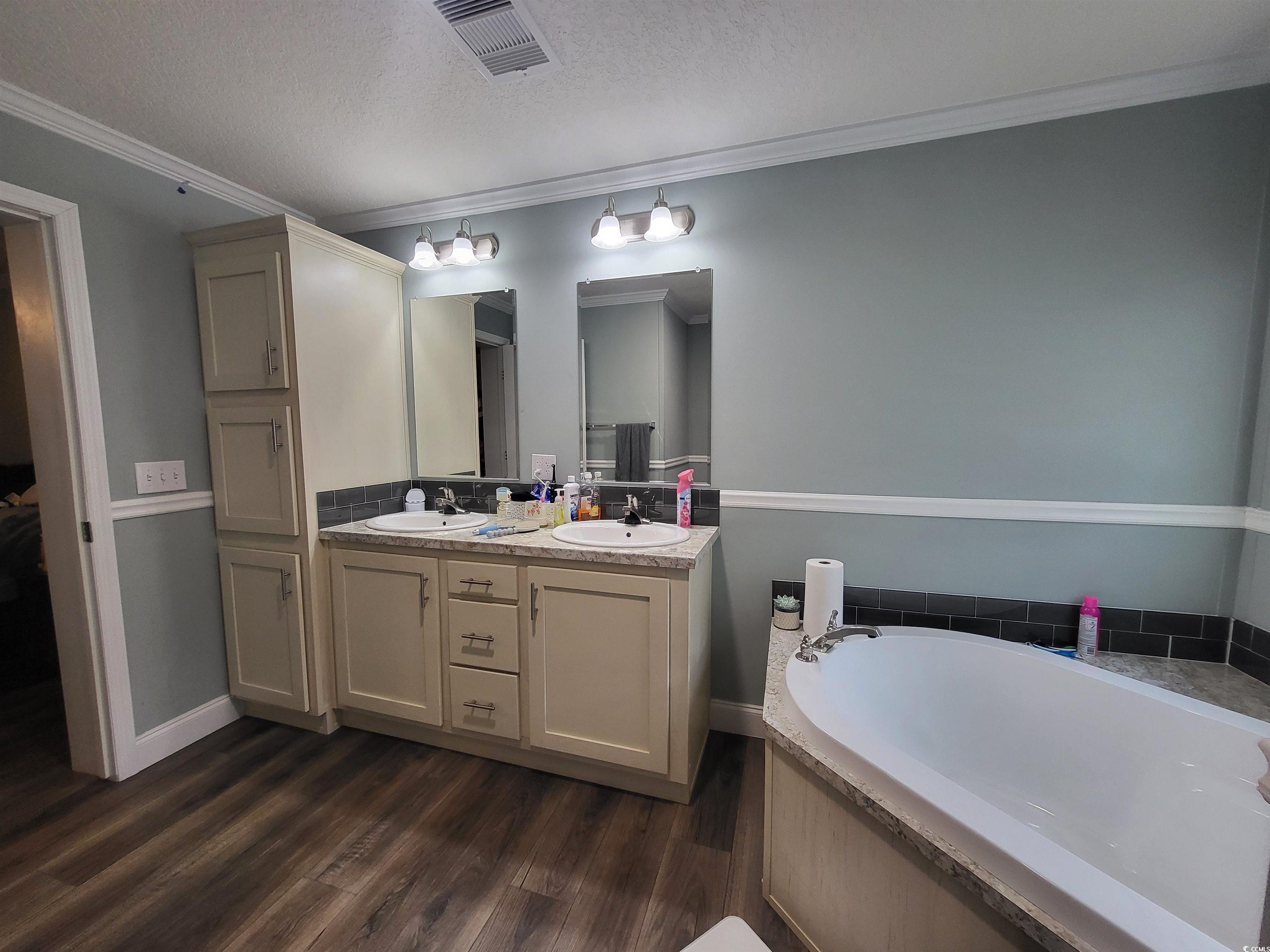 181 Offshore Drive Murrells Inlet, SC 29576 - Photo 13 of 28 Mstr Bathroom featuring crown molding, double vanity, a garden tub, a textured ceiling, and dark wood-style floors